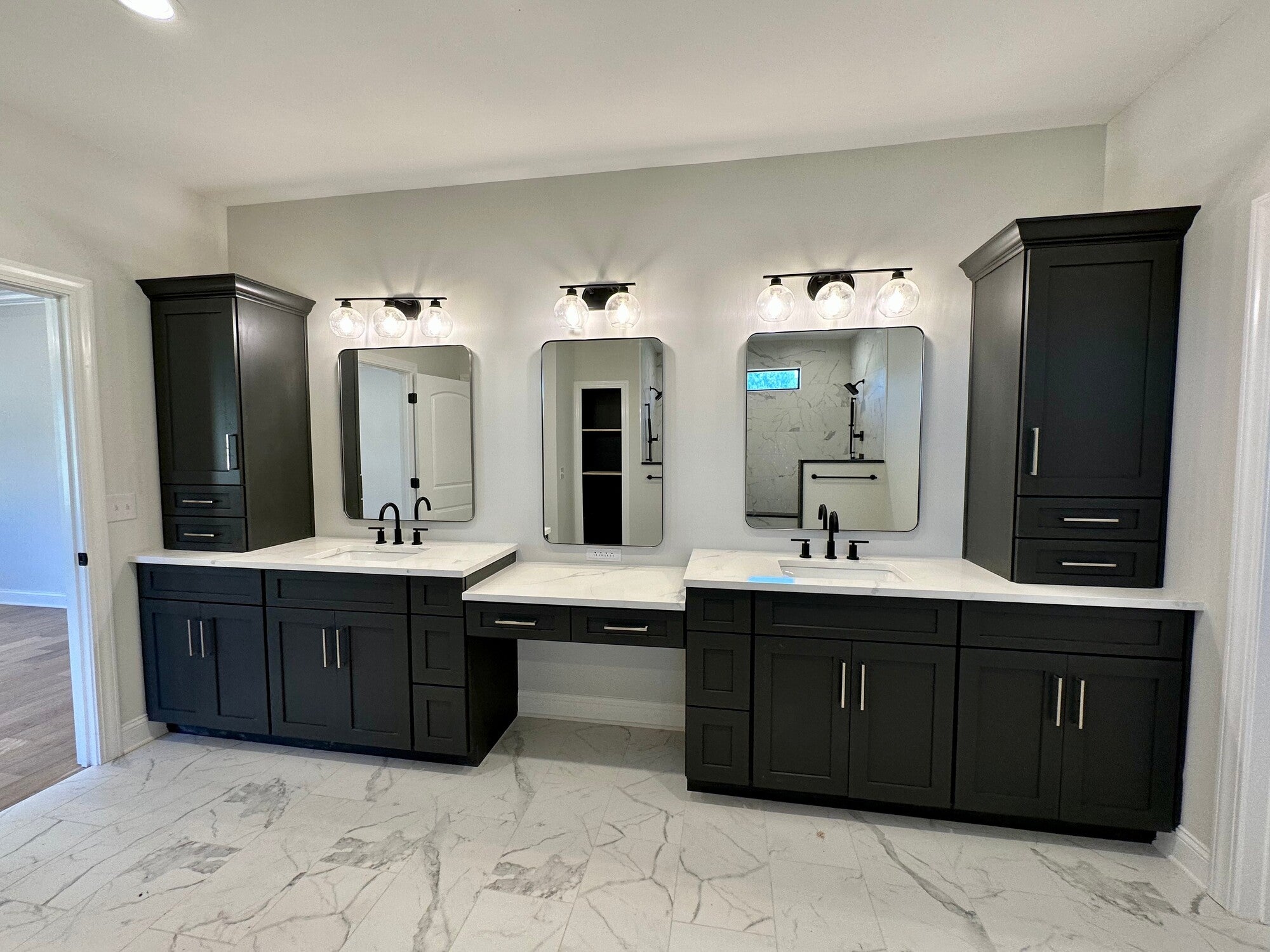 Modern bathroom with black cabinets, white countertops, dual sinks, three mirrors, and globe light fixtures highlighting the marble floor.
