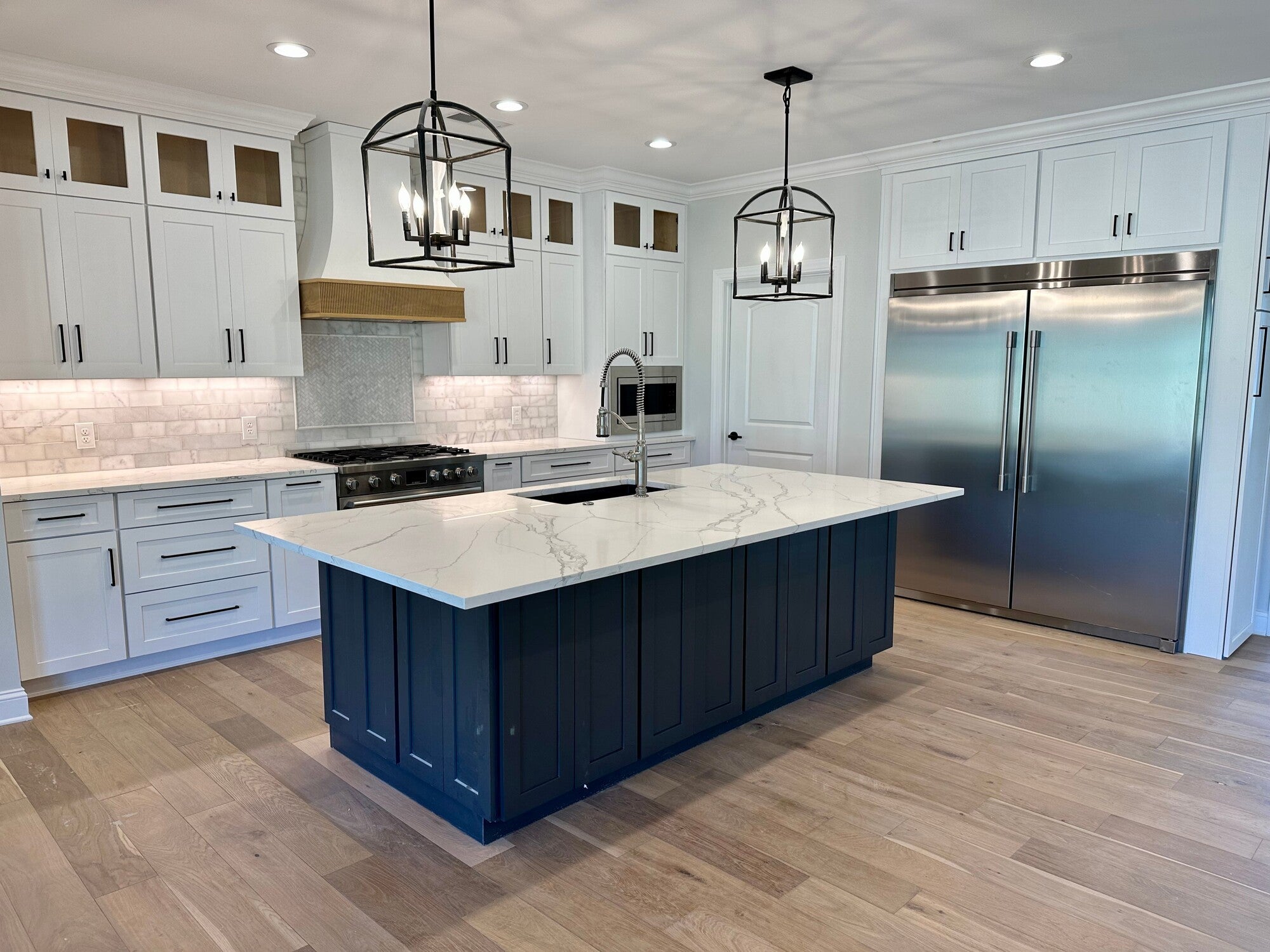 Modern kitchen with a marble island, dark blue base, stainless steel appliances, and white cabinets.